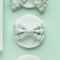 Matcha green textured tweed bow tie on a marble coaster, set against a pale green background.