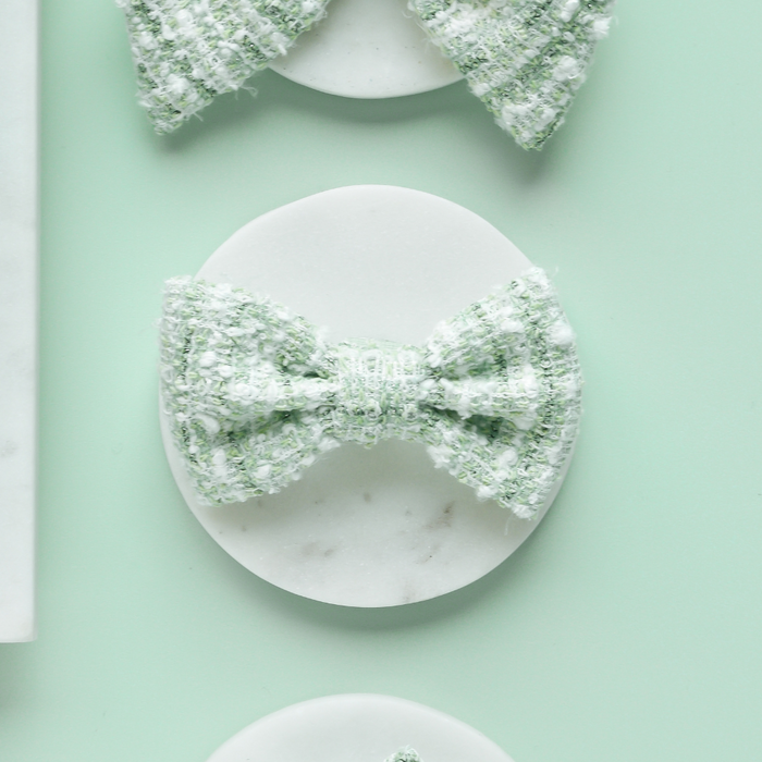 Matcha green textured tweed bow tie on a marble coaster, set against a pale green background.