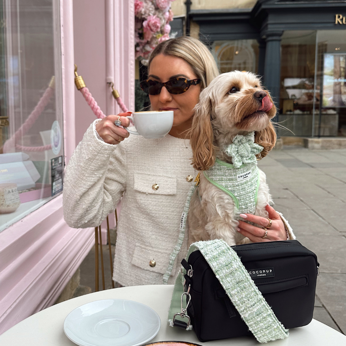Woman wearing sunglasses drinks coffee outside; her dog sports a green textured tweed collar flower.