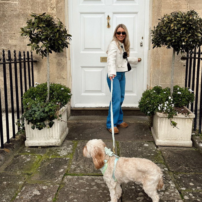 Woman in sunglasses holds a green textured tweed dog lead by Cocopup London, standing near a white door with plants.