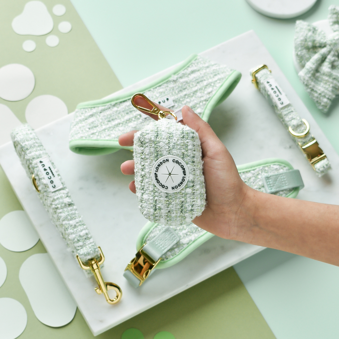 Hand holding a green textured tweed poop bag holder, with matching tweed dog accessories on a marble tray.