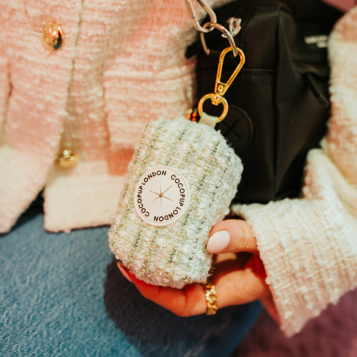 Matcha green tweed Cocopup London poop bag holder keychain pouch attached to a black bag, held by a hand.
