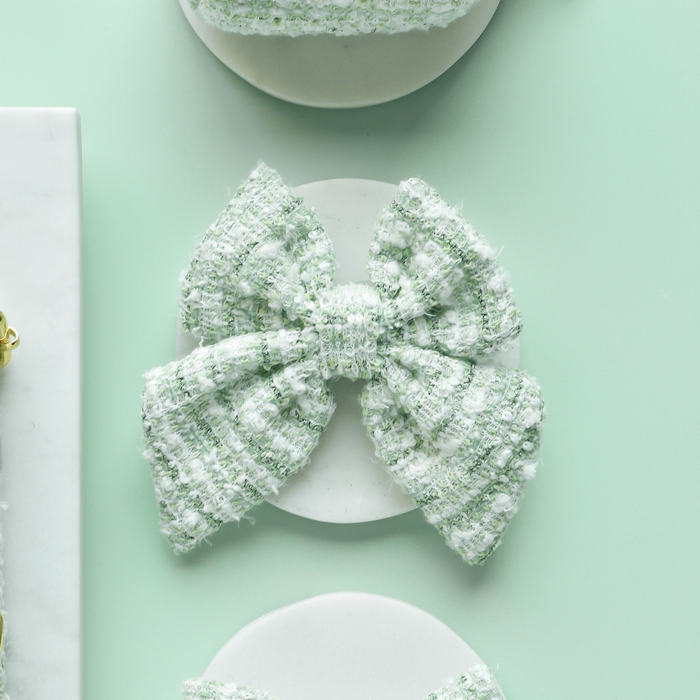 Matcha green textured tweed sailor bow tie on a white plate, set against a pastel green background.