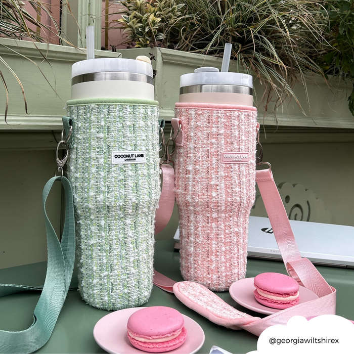 Two textured cups with lids next to pink macarons and a green tweed tumbler case.