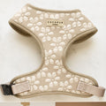 The Luxe Adjustable Neck Harness - Mocha Flower from Cocopup London is showcased on a light surface. This beige harness is adorned with white embroidered flowers and features a label that reads "Cocopup London." With adjustable straps and a black clasp on one side, it offers both style and functionality for your pup.