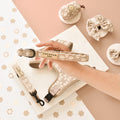 Hand holding a mocha floral Cocopup London collar, with matching pet accessories on a pink background.