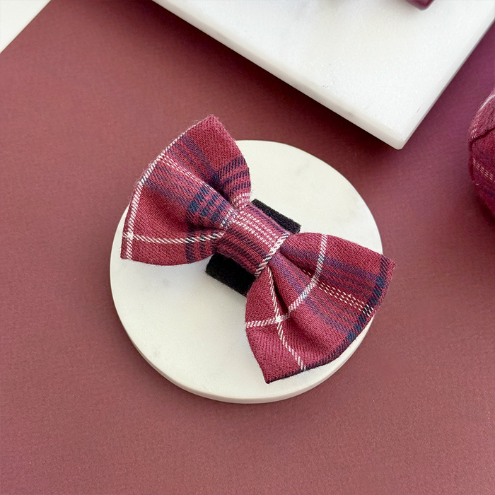 Plaid mulberry bow tie by Cocopup London displayed on a round white platform against a maroon background.