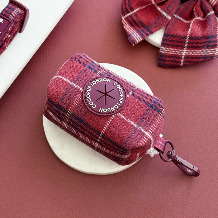 Mulberry plaid poop bag holder with white base, purple label, and matching plaid bow next to it.