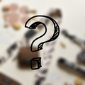 A large black hand-drawn question mark occupies the center of the image, set against a blurred background with indistinguishable objects. The image evokes a sense of mystery or inquisitiveness, much like our Cocopup London's Mystery Bag Strap featuring an adjustable length for added versatility.