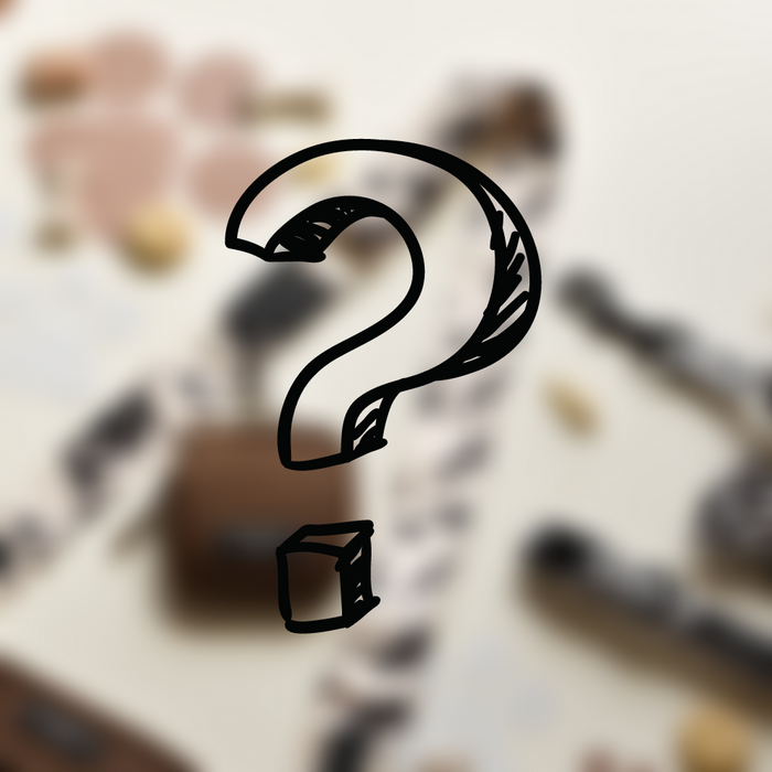 A large black hand-drawn question mark occupies the center of the image, set against a blurred background with indistinguishable objects. The image evokes a sense of mystery or inquisitiveness, much like our Cocopup London's Mystery Bag Strap featuring an adjustable length for added versatility.