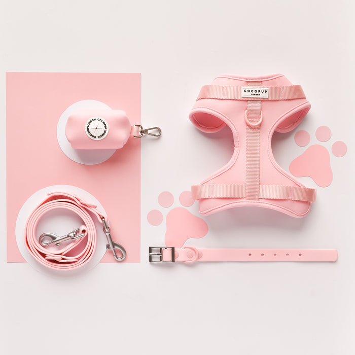Light pink Cocopup London NAKD Candyfloss harness, lead, collar, and poop bag holder on paw print background.
