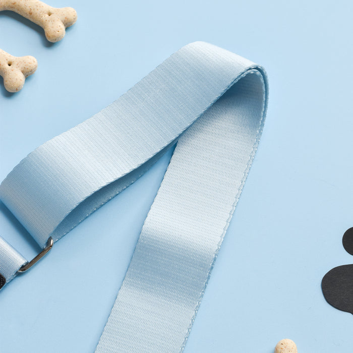 A light blue dog leash is laid out on a pastel blue surface. Surrounding it are dog bone-shaped treats and pieces of a black paw print cutout, creating a playful and pet-friendly scene, completed by the stylish Cocopup London Dog Walking Bag featuring the durable polyester NAKD Bag Strap in Bubblegum.