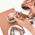 Hand holding a brown Cocopup London dog collar above matching dog accessories on a white and brown background.