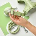 Hand holding a green Cocopup London NAKD Collar, with matching green leash and harness next to it.