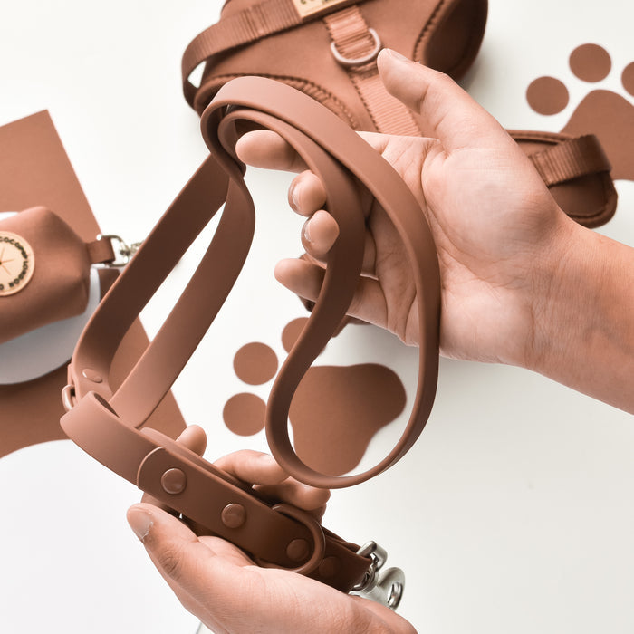 Hands hold a brown Cocopup London NAKD dog lead with a sturdy metal clasp.