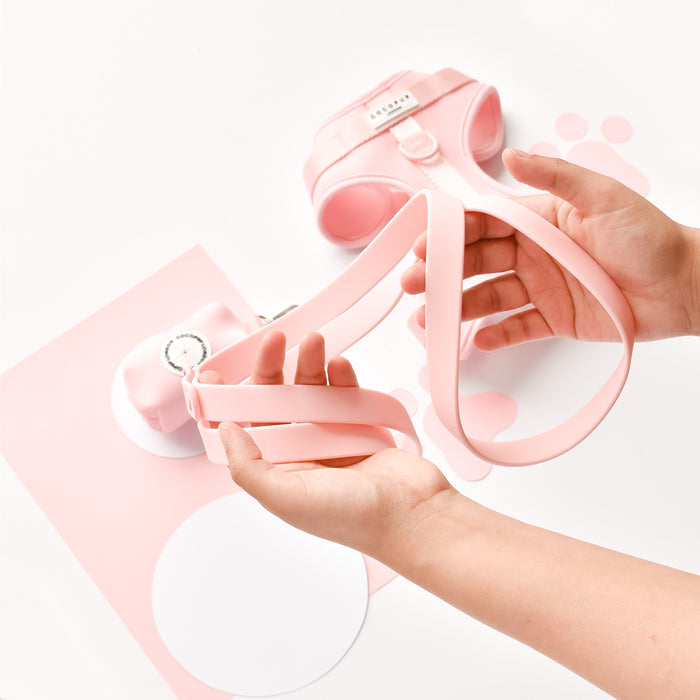 Hands hold a pink Cocopup London NAKD Lead beside a matching pink harness and accessories on a white background.
