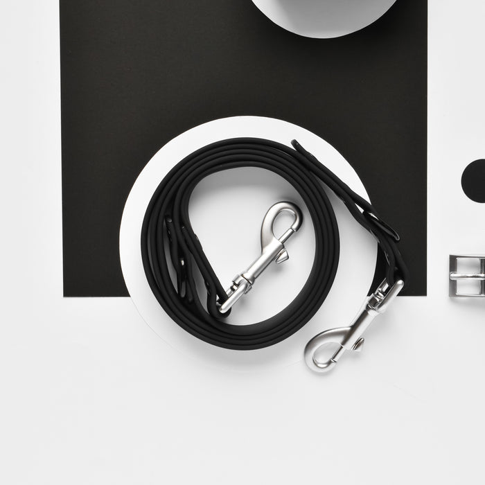 Black Cocopup London NAKD dog leash with metal clasps on a black and white geometric background.