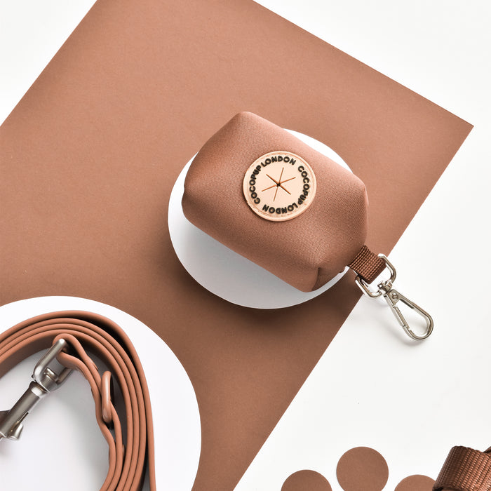 Brownie-colored Cocopup London NAKD poop bag holder with lobster clasp beside a rolled leash.