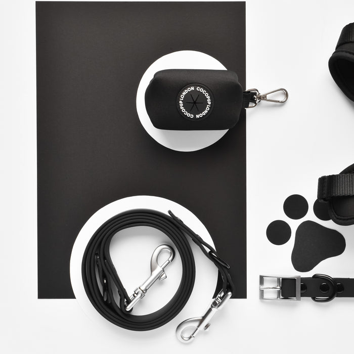 Black Cocopup London NAKD Poop Bag Holder, black leash, harness, and matching pet accessories arranged flat.