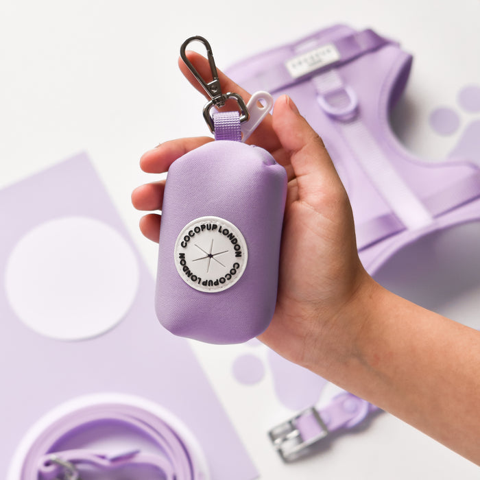 Hand holding a purple Cocopup London NAKD poop bag holder, with matching accessories in the background.