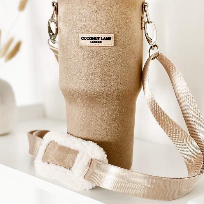Nude tumbler carry case with cross-body strap and shoulder pad, displayed on a white surface.