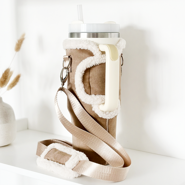 Beige tumbler carry case with straw and cross-body strap displayed on a white shelf.