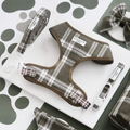 Olive check harness, lead and collar set from Cocopup London displayed on marble with a paw print patterned background.