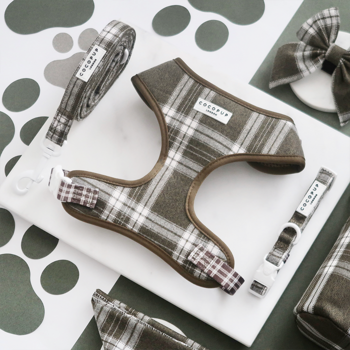 Olive check harness, lead and collar set from Cocopup London displayed on marble with a paw print patterned background.