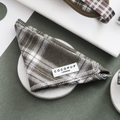 Olive green checkered bandana from Cocopup London displayed on a round white dish.
