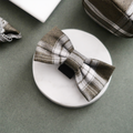 Olive check bow tie with black center band, displayed on a white circular coaster.