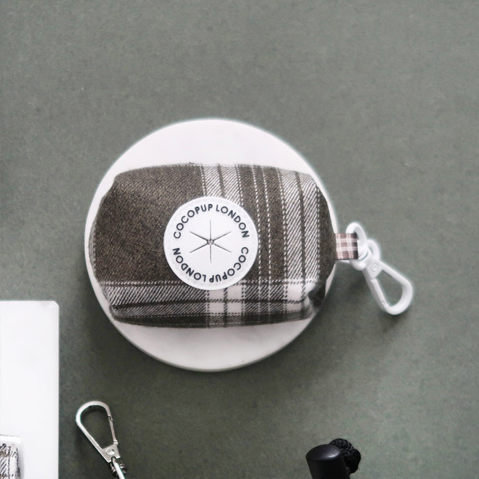 Olive checkered poop bag holder with metal clip attached to a round white dish.