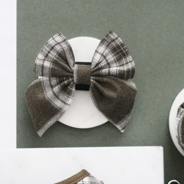 Olive check sailor bow tie by Cocopup London on a white circle, placed on a green background.