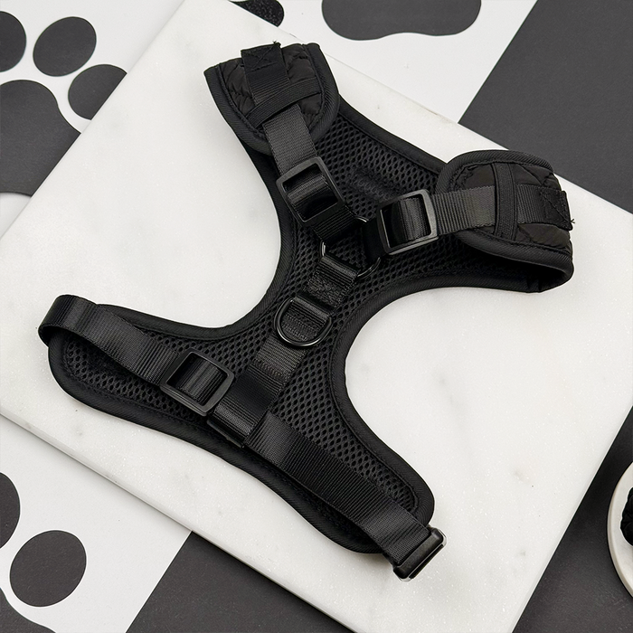 Black quilted adjustable neck harness by Cocopup London on a white background with paw print pattern.