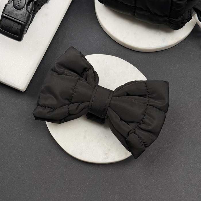 Black quilted bow tie for dogs by Cocopup London, displayed on a white marble surface.