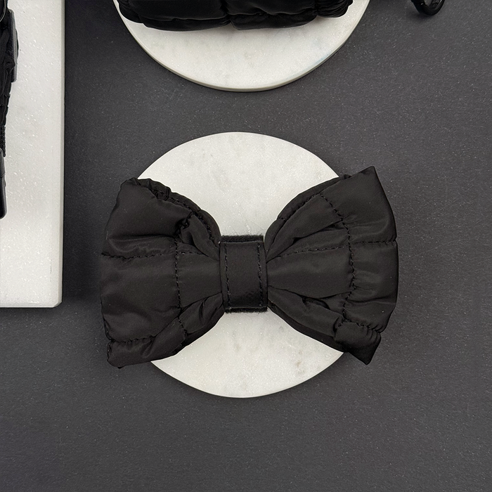 Black quilted bow tie by Cocopup London on a white marble surface.