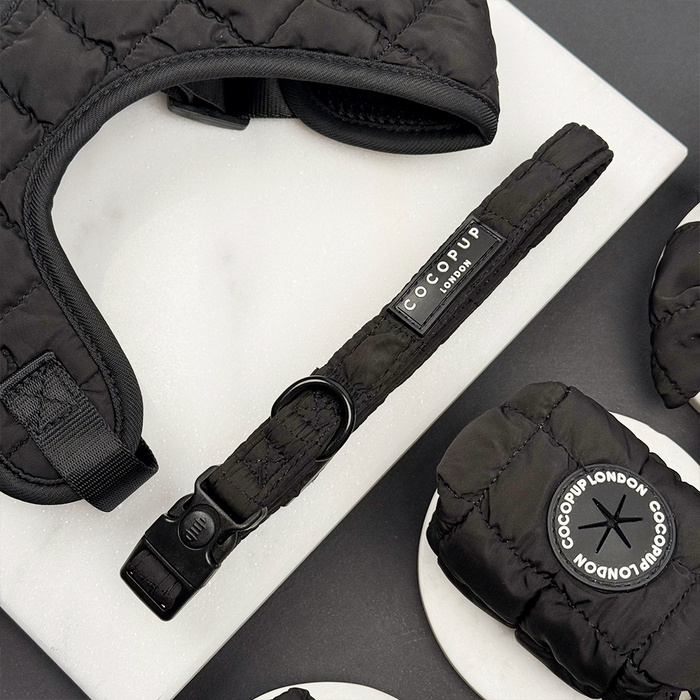 Black quilted dog collar with matching accessories from Cocopup London on a white marble background.