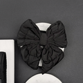 Large black quilted sailor bow tie by Cocopup London resting on a white stone with a dark background.