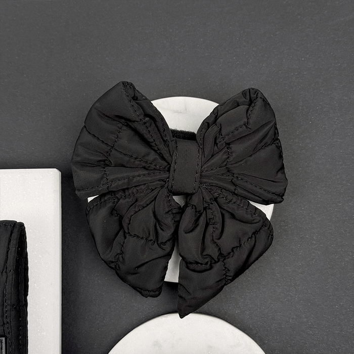 Large black quilted sailor bow tie by Cocopup London resting on a white stone with a dark background.