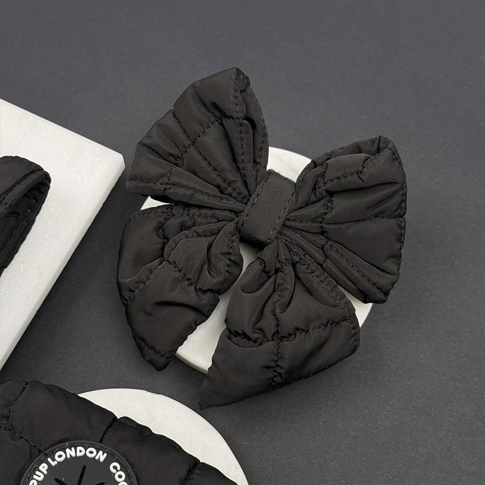Black quilted sailor bow tie with a textured finish sits on a gray circle next to other quilted accessories.