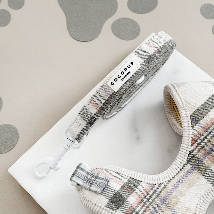 Oxford plaid harness, lead and collar bundle on a marble slab with paw prints in the background.