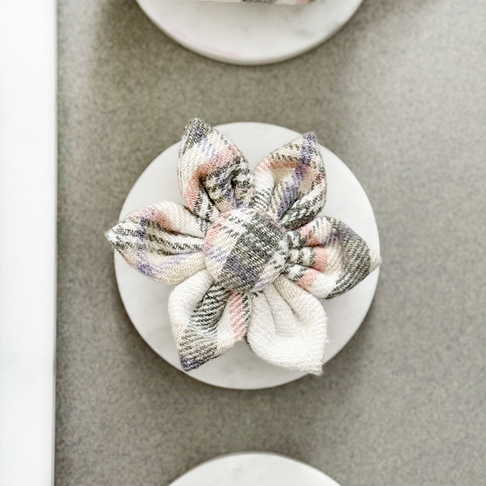 Oxford plaid dog collar flower in muted tones displayed on a round white surface with a gray background.