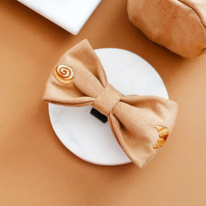 Tan suede Pawtisserie Bow Tie by Cocopup London with embroidered designs on a white marble and tan surface.