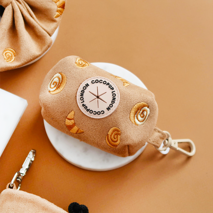 Tan poop bag holder with croissant embroidery and a metal key clip.