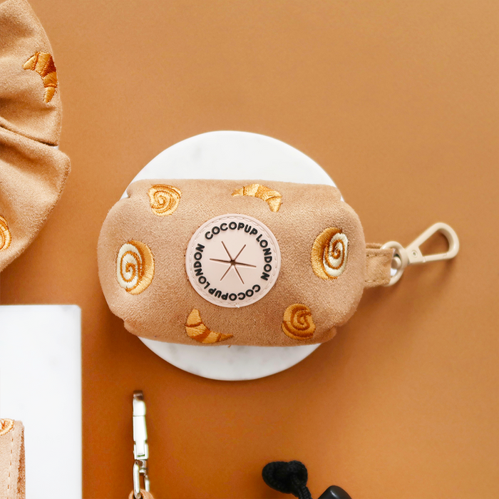Tan Cocopup London poop bag holder with yellow swirl pattern, metal clip, and logo patch on a brown backdrop.