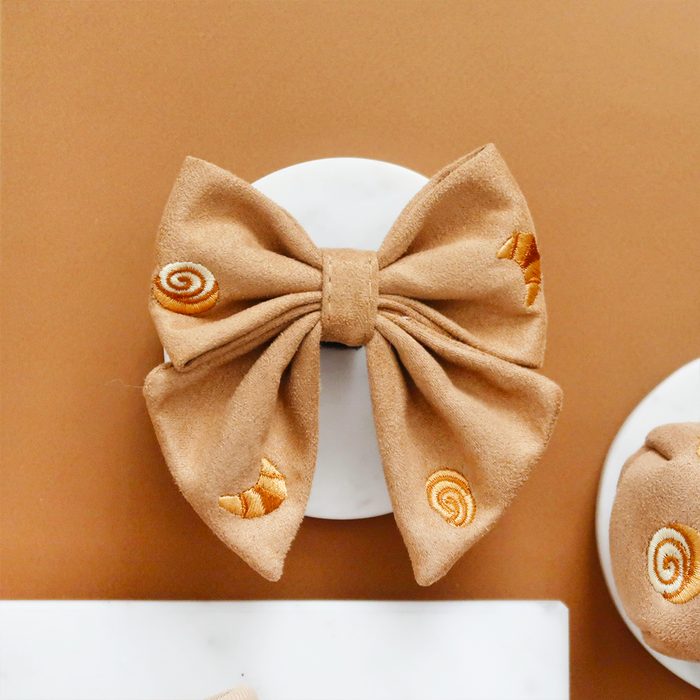 Tan Cocopup London Pawtisserie Sailor Bow Tie with croissant and pastry swirl pattern on a white surface, brown background.