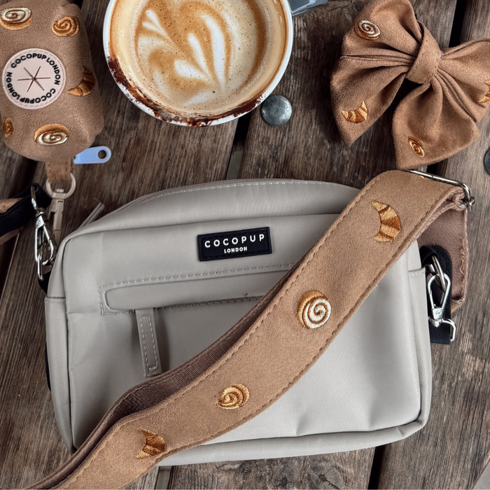 Beige Cocopup London bag with pastry-patterned strap, Pawtisserie Sailor Bow Tie, and latte on rustic wood table.