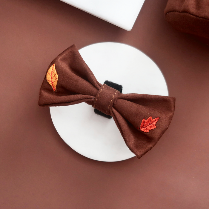Brown fabric bow tie with orange leaf embroidery from Cocopup London, displayed on a white round surface.