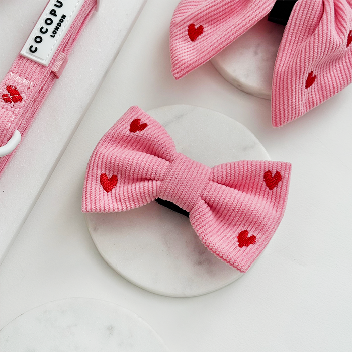 Pink cord bow tie with ribbed texture and red heart print, paired with a matching embroidered bow.