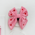 Pink cord sailor bow tie with red hearts pattern from Cocopup London on a white round surface.