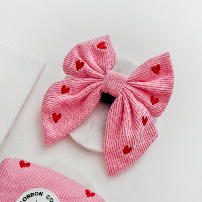 Pink cord sailor bow tie with red hearts, displayed beside a marble coaster and Cocopup London label.